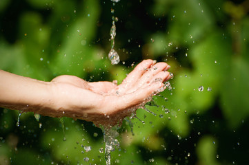 Fototapeta na wymiar Woman washing hand outdoors. Natural drinking water in the palm. Young hands with water splash, selective focus