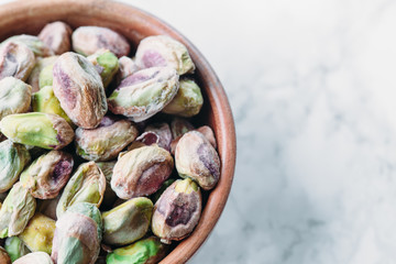 Pistachios in wooden bowl on marble background with copy space 