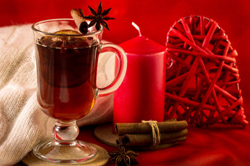Mulled wine with cinnamon and candle on red background