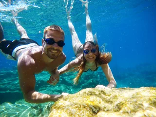 Wall murals Diving Underwater photo of young cute romantic love couple exploring and enjoying with goggles in the exotic turquoise sea near the coral reef while holding hands together.
