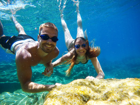 Underwater photo of young cute romantic love couple exploring and enjoying with goggles in the exotic turquoise sea near the coral reef while holding hands together.