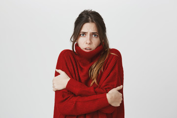 Waist-up portrait of girl suffering from physical discomfort because of fever. Dark-haired woman with ponytail dressed in red loose sweater feels cold in winter