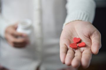 Female hands is holding red pills in heart shape.