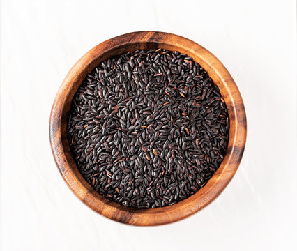 Isolated handful of raw black (nero) rice in the wood bowl on white background