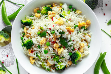 Fried rice with vegetables, broccoli, peas and eggs in a white bowl. soy sauce. healthy food