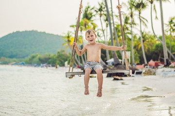Happy boy sit on swing at the sea shore on sunset