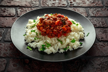 Homemade beef mince and vegetable casserole served with rice on black plate.