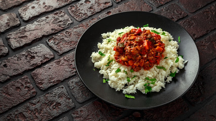 Homemade beef mince and vegetable casserole served with rice on black plate.