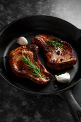 Cooked Pork Loin chops in rustic skillet, pan with rosemary. top view. background