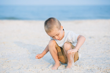 Fototapeta na wymiar Portrait serious little boy playing in the sand near the sea, ocean. Positive human emotions, feelings, joy. Funny cute child taking vacations and enjoying summer.