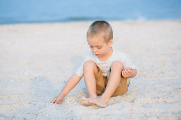 Portrait serious little boy playing in the sand near the sea, ocean. Positive human emotions, feelings, joy. Funny cute child taking vacations and enjoying summer.