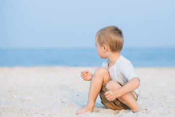 Fototapeta na wymiar Little boy playing in the sand near the sea, ocean. Positive human emotions, feelings, joy. Funny cute child taking vacations and enjoying summer.