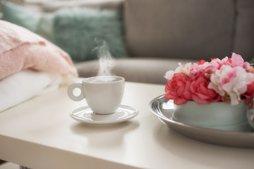 Still life details in home interior of living room. Sweaters and cup of coffe with steam on a serving tray on a coffee table. Breakfast over sofa in morning sunlight.