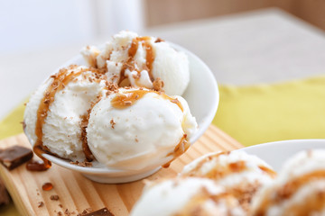 Tasty vanilla ice-cream balls with caramel topping in bowl on board