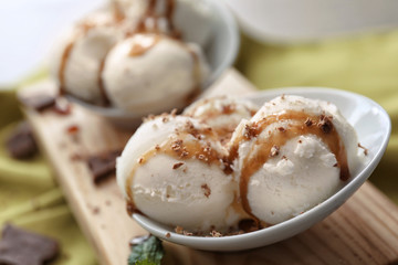 Tasty vanilla ice-cream balls with caramel topping in bowl on board