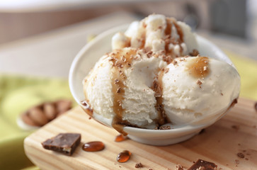 Tasty vanilla ice-cream balls with caramel topping in bowl on board