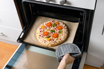 Woman putting baking sheet with pizza in oven