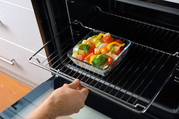 Man putting glass baking dish with vegetables in oven