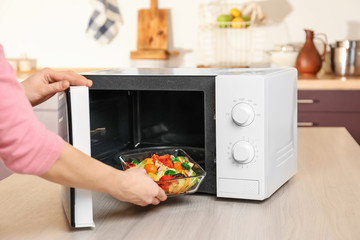 Woman putting bowl with vegetables in microwave oven, closeup - obrazy, fototapety, plakaty