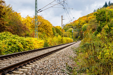 Fototapeta premium A railway track in Freiburg im Breisgau on a very stormy autumn day. The vibrant colors of the trees are in big contrast with the grey stones of the track. The track leads the picture from the left