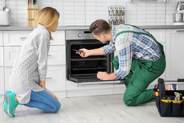 Housewife with worker near oven in kitchen