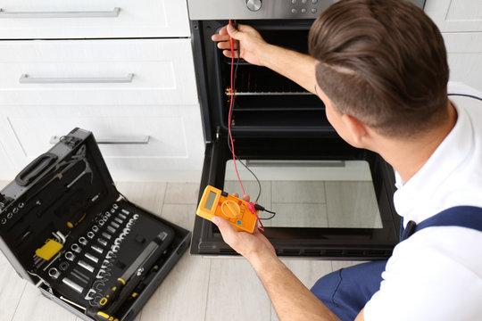 Young man with multimeter repairing oven in kitchen