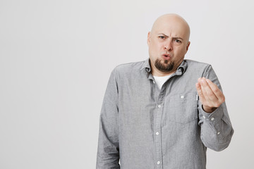 Horizontal portrait of dissatisfied and displeased bald man with beard dressed casually, gesturing...