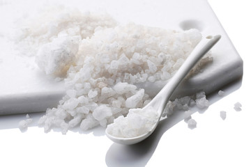 a pile of sea salt with a ceramic spoon on a white background. isolate.