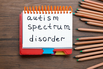 Notebook with phrase "Autism spectrum disorder" on wooden background