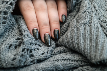 Fototapeta na wymiar Beautiful winter manicure. Black lacquer with luster and white patterns of snow and frost. The gray background is also with beautiful curled drawings
