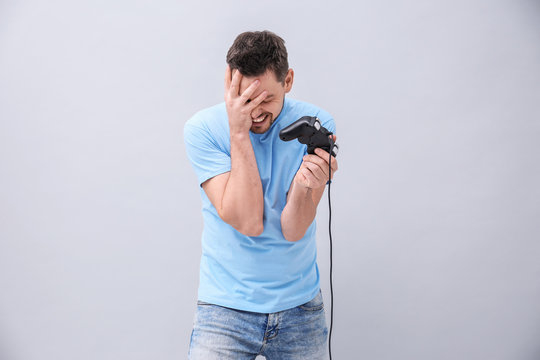 Upset man with video game controller on grey background
