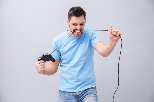 Angry man with video game controller on grey background