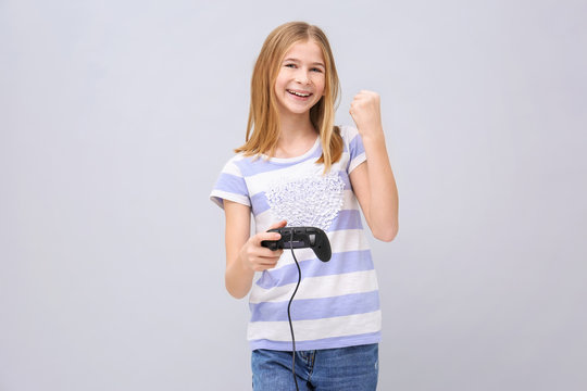 Happy teenage girl with video game controller on grey background