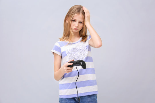 Upset teenage girl with video game controller on grey background