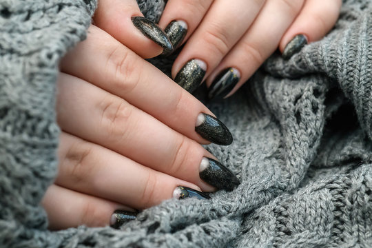 Beautiful winter manicure. Black lacquer with luster and white patterns of snow and frost. The gray background is also with beautiful curled drawings