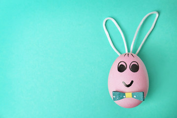 Easter egg decorated with bunny ears on color background
