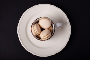Vanilla macarons in a white cup, black background