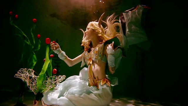 young girl in the elf costume is kept under water in the darkness illuminates the light. role play.