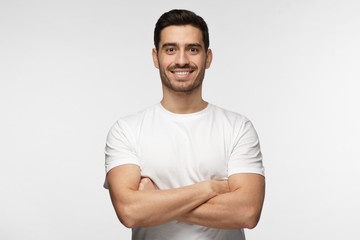 Portrait of smiling handsome man in white tshirt standing with crossed arms isolated on grey background