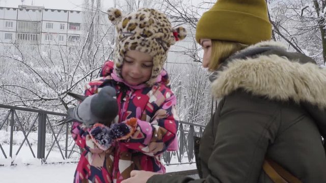 Mom and daughter are feeding pigeons in a winter park
