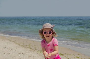 Little funny girl (3 years old) at the sea in pink sunglasses.