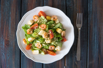 Caesar salad with shrimps in a white plate top view