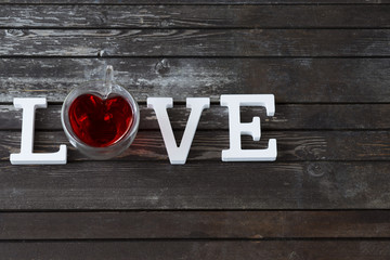on a wooden dark table a cup of red tea and the word love from white wooden letters