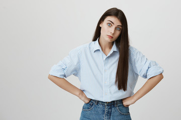 Portrait of irritated and annoyed young woman, holding hands on waist, looking with wide eyes,...