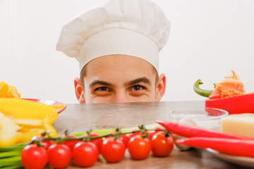 Man with cook cap on white background. Chef with vegetables on table. Cook with cheerful face in face close up.