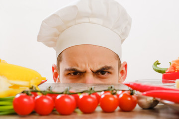 Man with cook cap on white background. Chef with vegetables on table. Cook with cheerful face in face close up.
