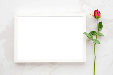 Valentine's day background, template, Red rose and blank white wooden frame on white marble background with copy space for text, flat lay
