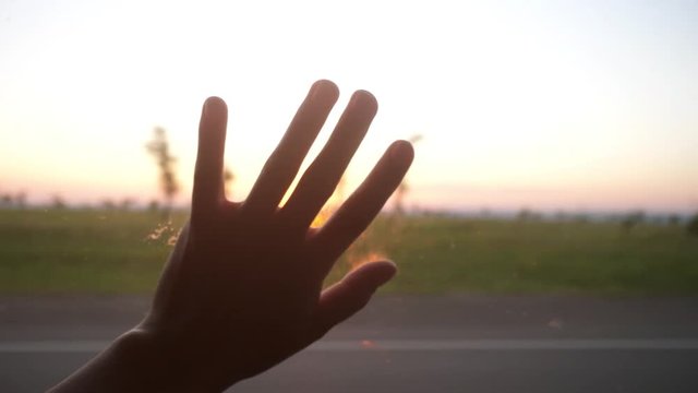 Female hand is playing with sun from car window against beautiful sunset. slow motion. 3840x2160