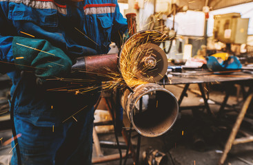 Profesional worker in protective uniform cutting metal pipe with electric grinder in the industrial...