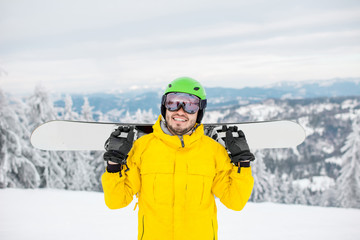 Fototapeta na wymiar Portrait of a man dressed in winter sports clothes holding a snowboard at the mountains